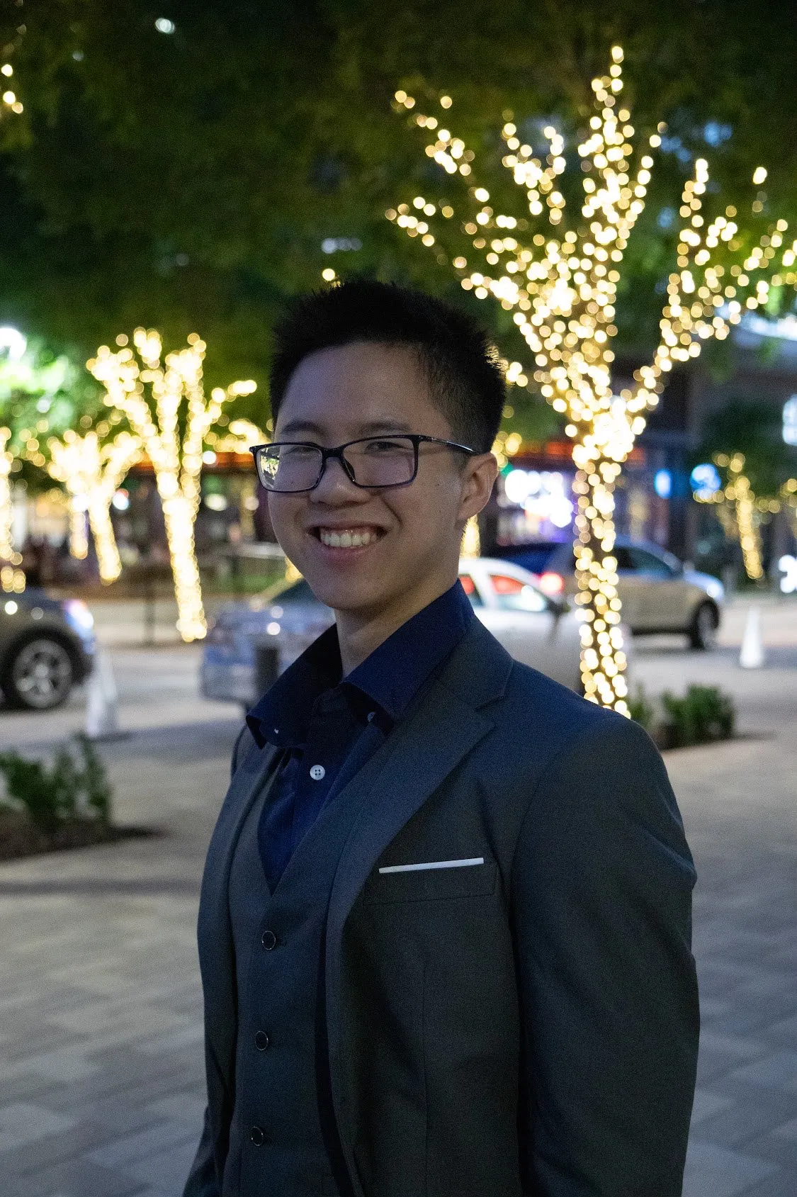 Sean in a grey suit, smiling, under trees strung with lights at night